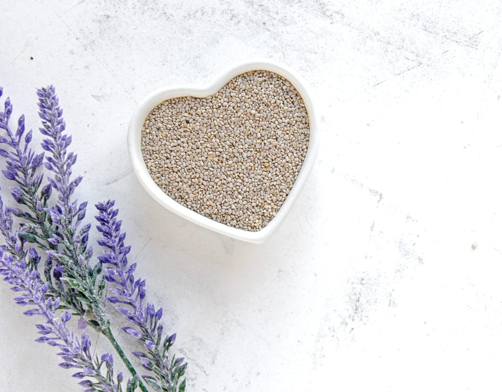 White chia seeds in a heart bowl on vintage white surface and la